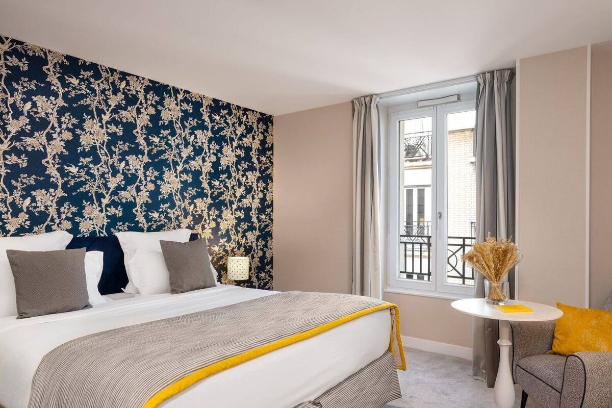 A hotel room with a large bed, a small table, and a view of the outside balcony.