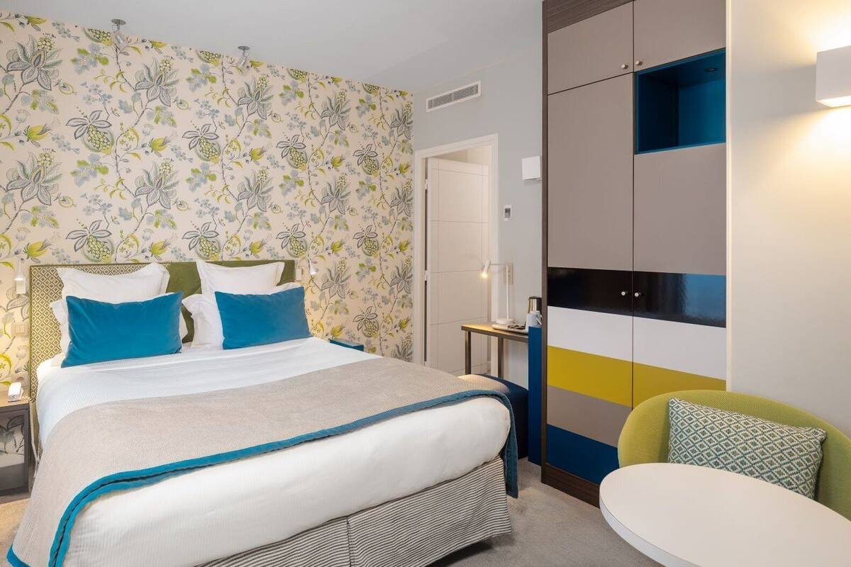A bedroom with a bed, bedside table, lamp, and a chair.