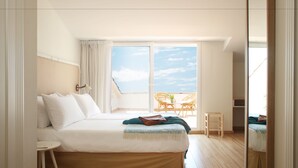 A bedroom with a large bed, a small table, a chair, and a balcony with wicker furniture.