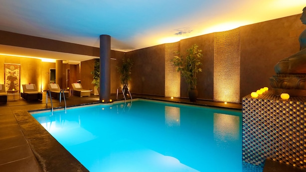A modern indoor pool area with a clear pool, lounge chairs, and a Buddha statue.