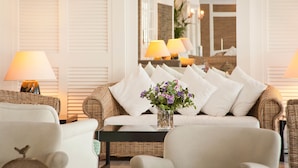 A cozy living room with a white sofa, two armchairs, a glass coffee table, and a vase with flowers.
