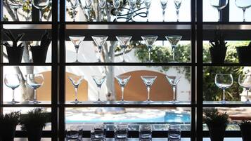 Una zona de bar con distintos tipos de vasos y botellas, incluyendo vasos de martini y copas de vino, organizados en estantes.