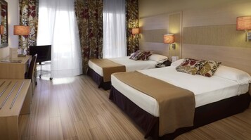 A hotel room with two beds, a desk, a chair, and a lamp.