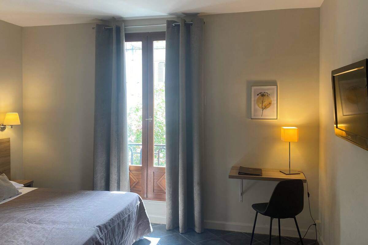 Une chambre d’hôtel comprenant un lit, un bureau avec une chaise, une fenêtre avec des rideaux et un tableau accroché au mur.