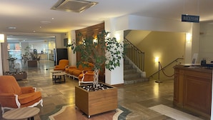 A lobby with a reception desk, a staircase, and seating areas. - Grand Hotel (Calvi)
