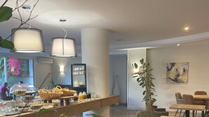 A modern dining area with a buffet setup, comfortable seating, and a large potted plant. - Grand Hotel (Calvi)