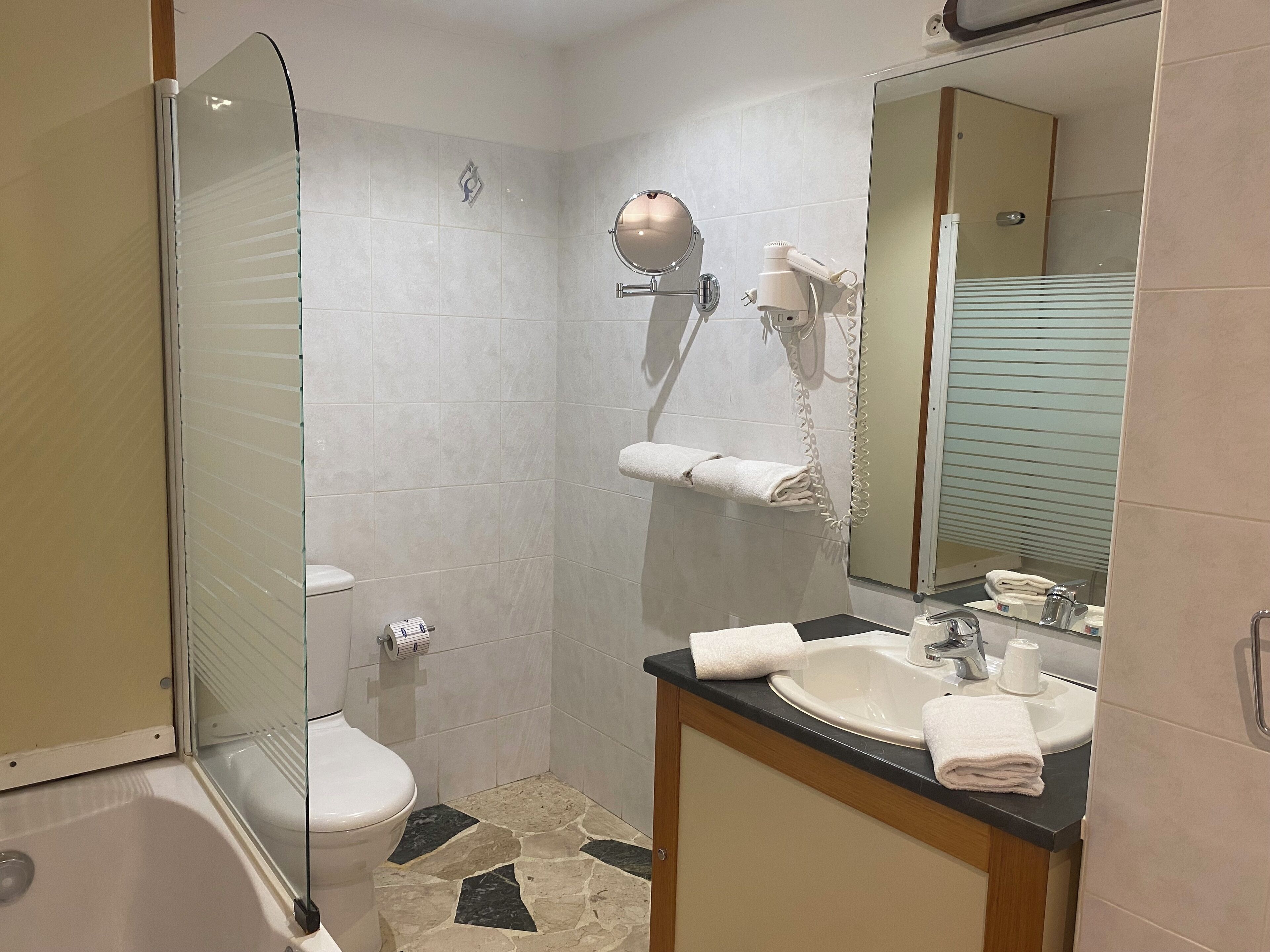 A bathroom with a toilet, a sink with a mirror, a towel rack, and a shower area.