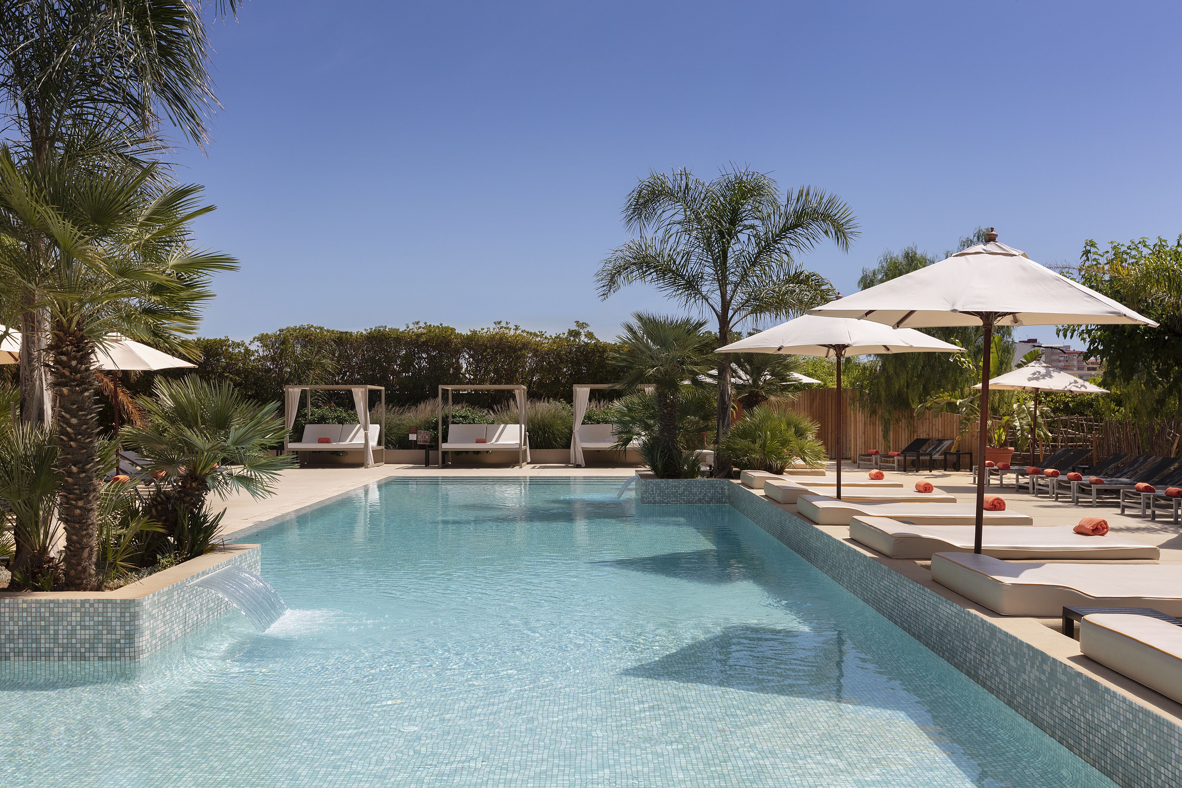 Une piscine entourée de palmiers et de verdure, avec des chaises longues et des parasols.