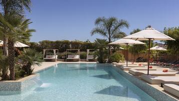Une piscine entourée de palmiers et de verdure, avec des chaises longues et des parasols.