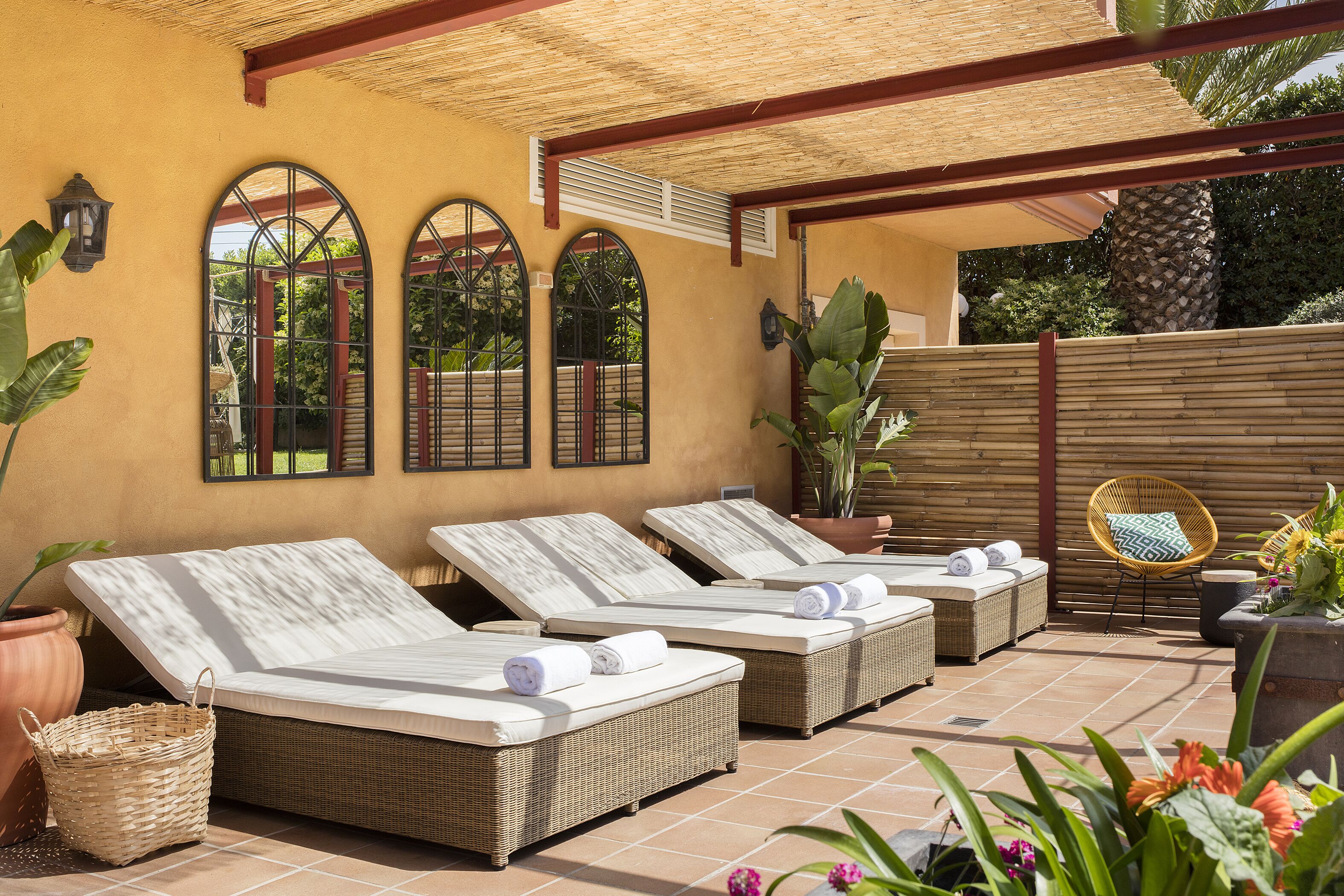 Un espace de détente extérieur, baigné de lumière, avec trois fauteuils en osier, chacun doté d’un coussin blanc et de serviettes enroulées.
