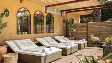 Un espace de détente extérieur, baigné de lumière, avec trois fauteuils en osier, chacun doté d’un coussin blanc et de serviettes enroulées.