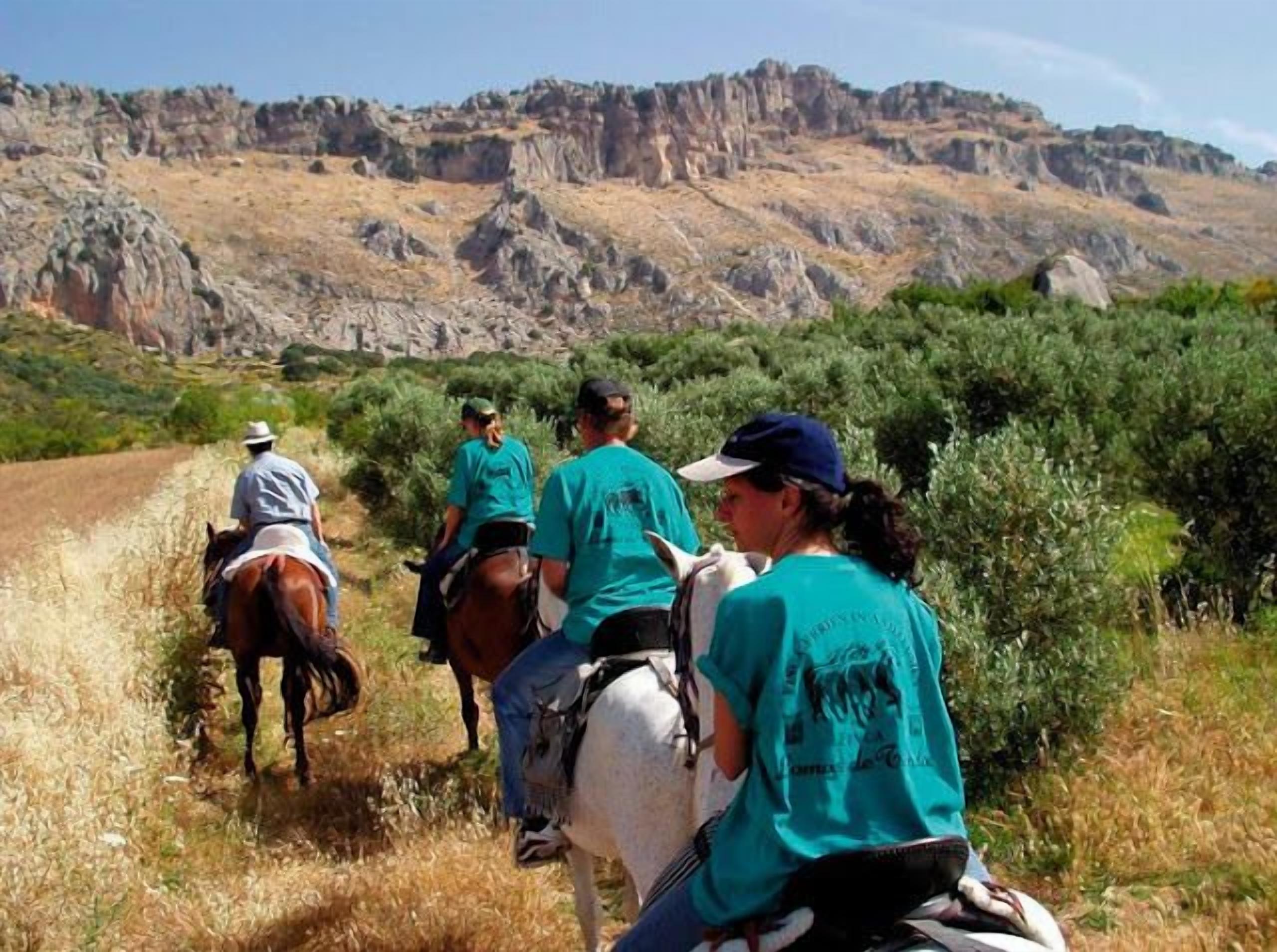 A group of people on horseback riding along a dirt path with rocky hills in the background.