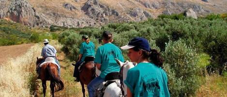 A group of people on horseback riding along a dirt path with rocky hills in the background.