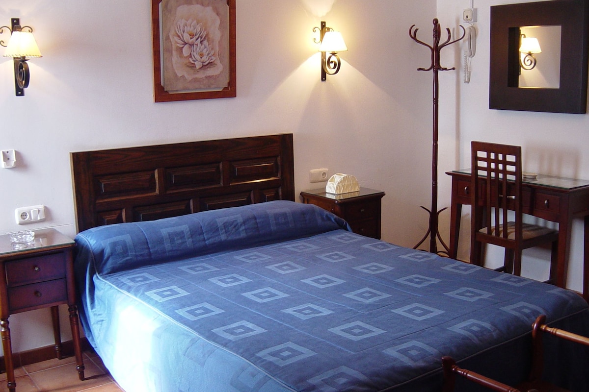 A hotel room with a bed, a desk, a chair, and wall-mounted lamps.