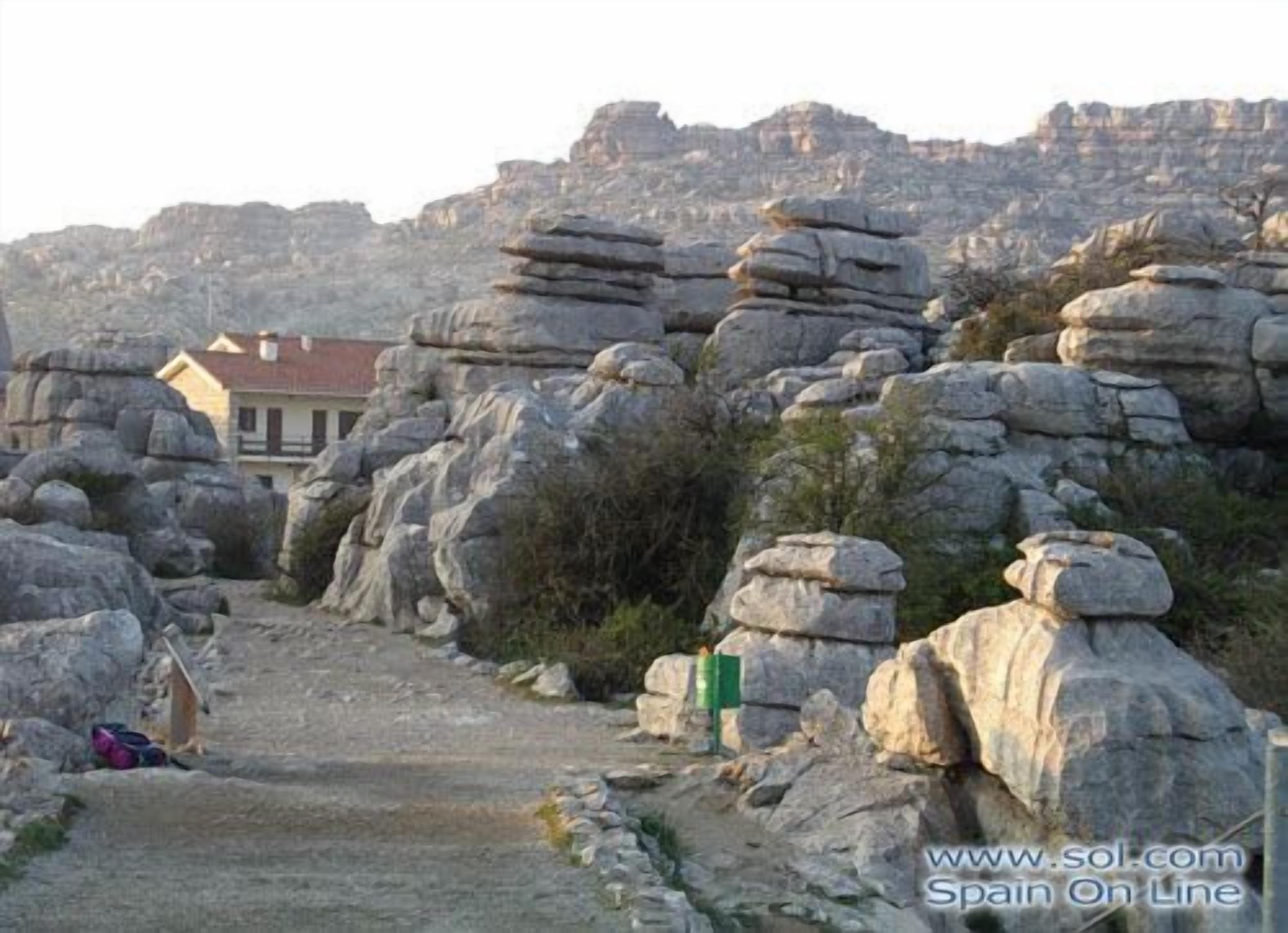 A rocky landscape with a path leading to a building with a red roof.
