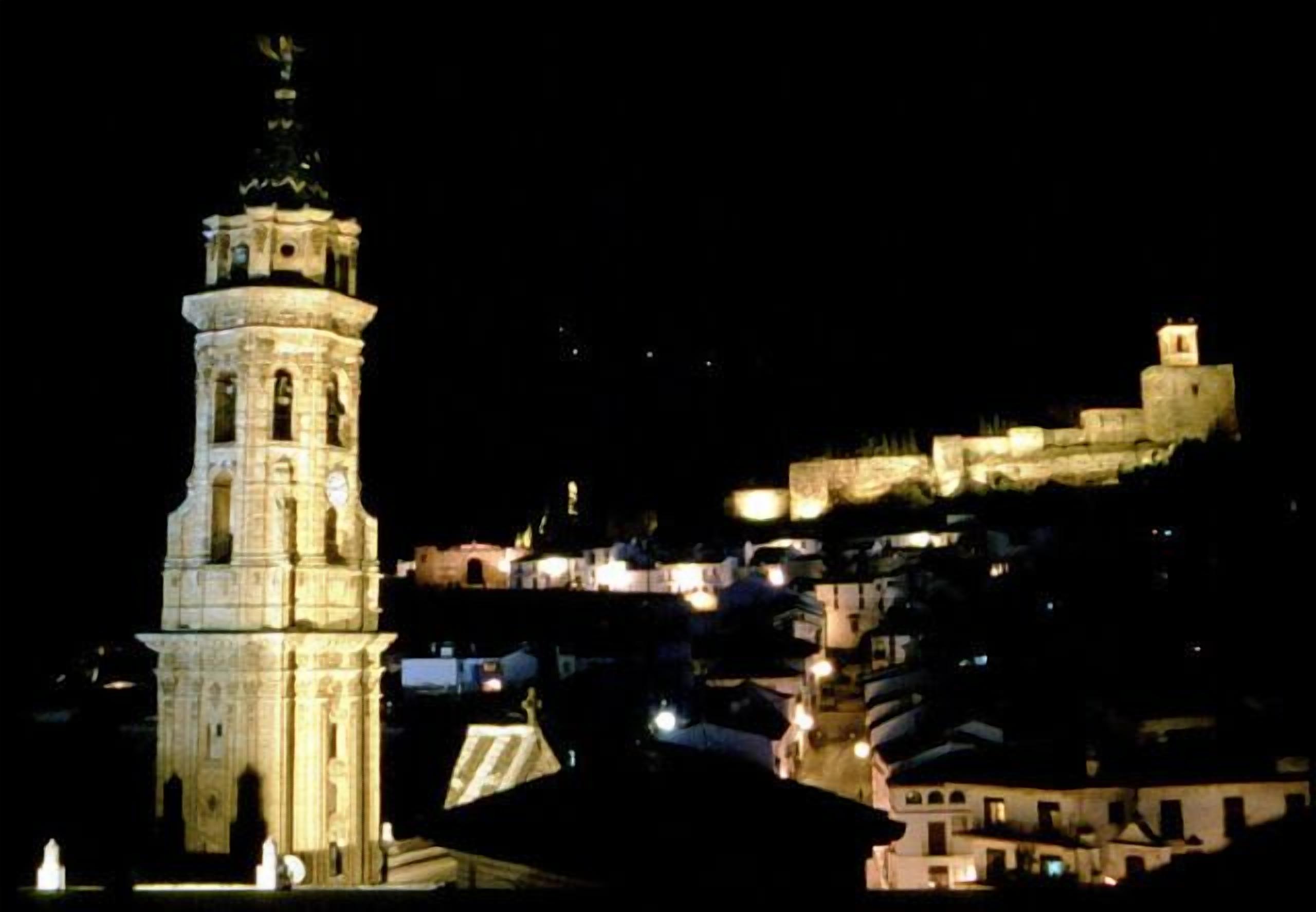 A historic tower with a clock, surrounded by buildings and a fortified wall.