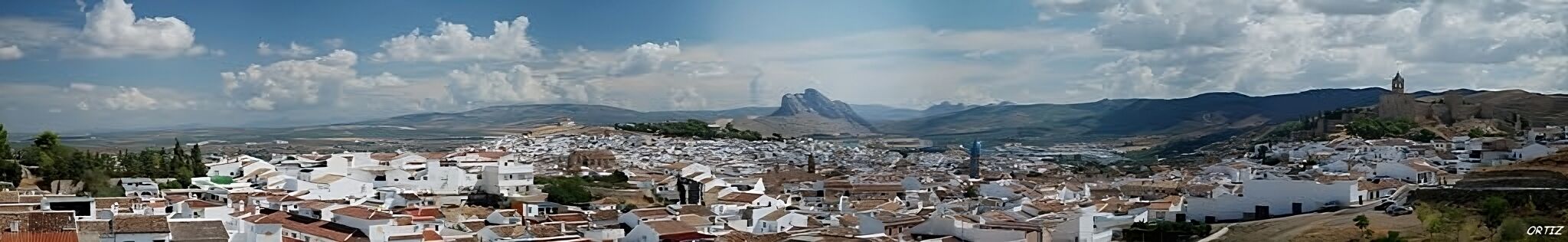 A town with white buildings and a prominent mountain in the background.