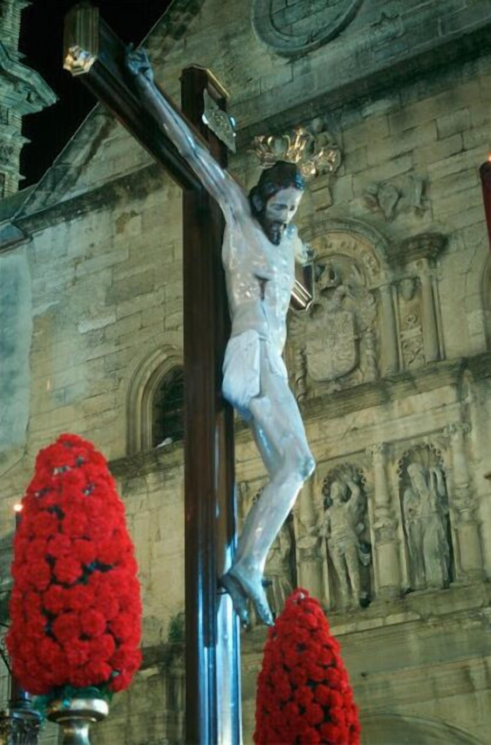 A crucifixion scene with a figure on a cross, set against a stone building with classical architecture.