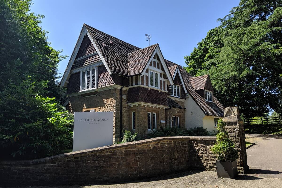 A Tudor-style building with a stone facade, multiple chimneys, and a sign reading "HARTSFIELD MANOR."