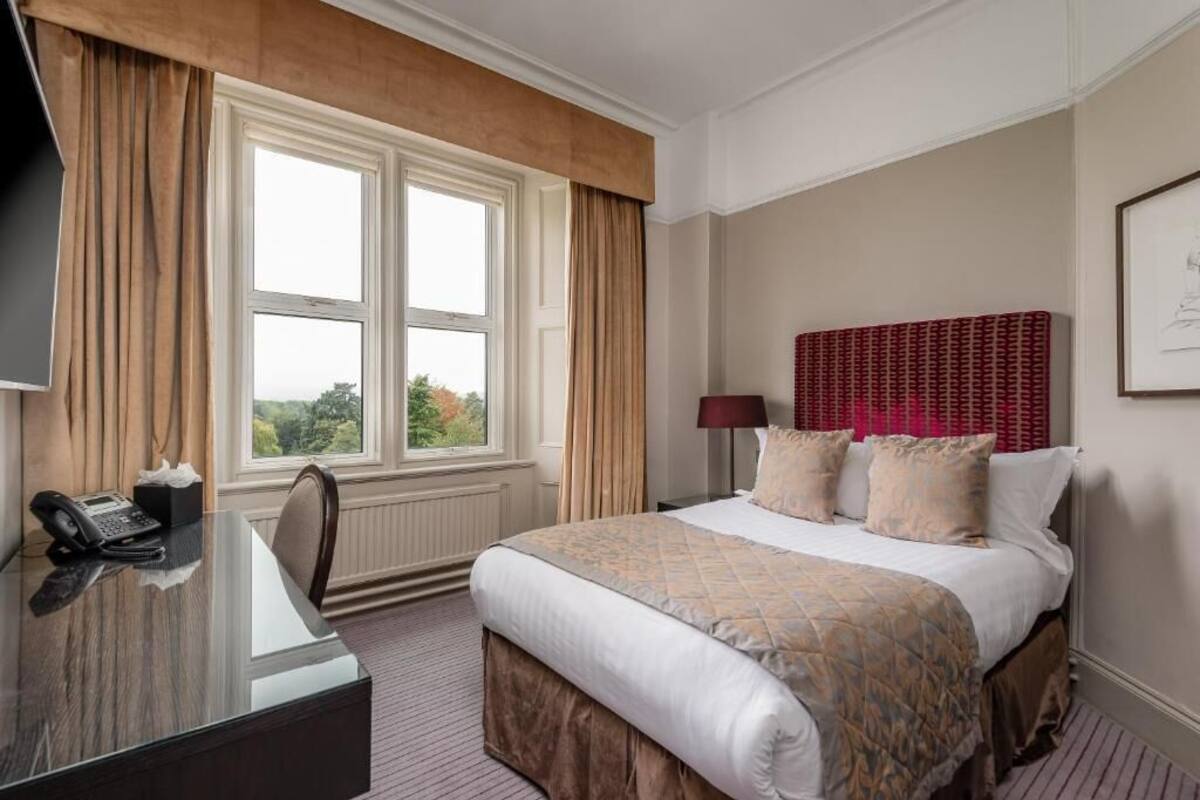 A hotel room with a large bed, a desk with a telephone, and a window with curtains.