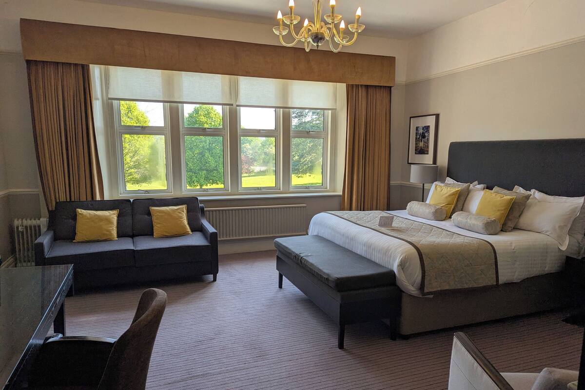 A hotel room with a large bed, a sofa, a chair, and a desk.