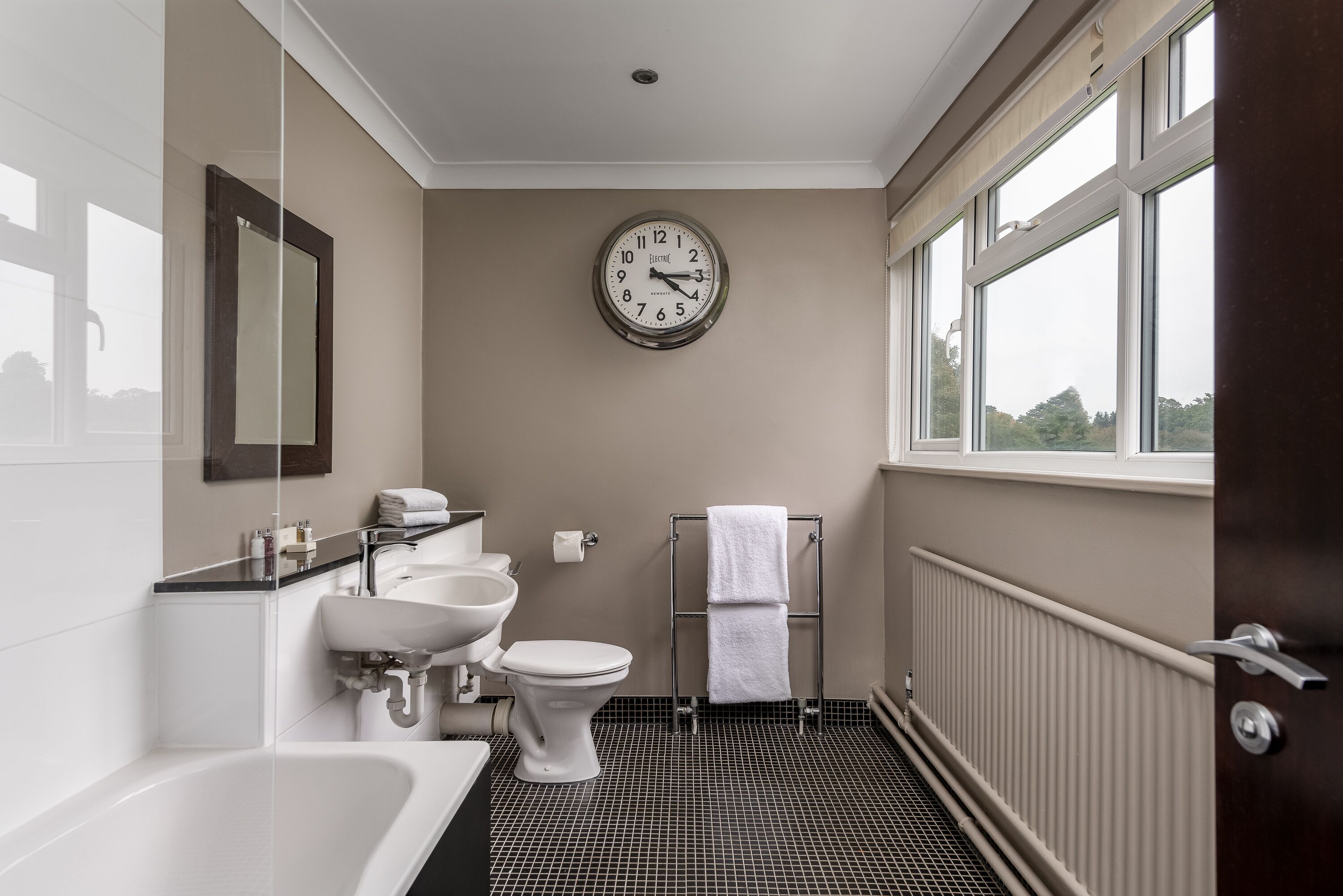 Un baño con bañera, lavabo, inodoro y un reloj en la pared.