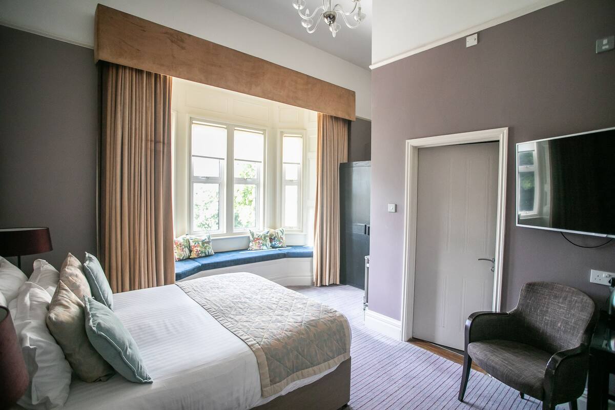 A hotel room with a large bed, a seating area by the window, a television, and a chair.