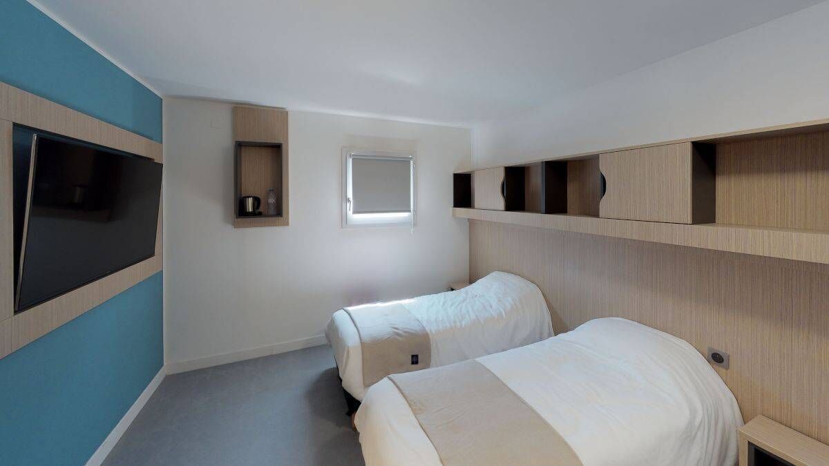 Een hotelkamer met twee bedden, een aan de muur bevestigde televisie, een raam en ingebouwde planken.