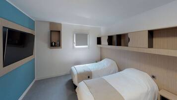 Een hotelkamer met twee bedden, een aan de muur bevestigde televisie, een raam en ingebouwde planken.