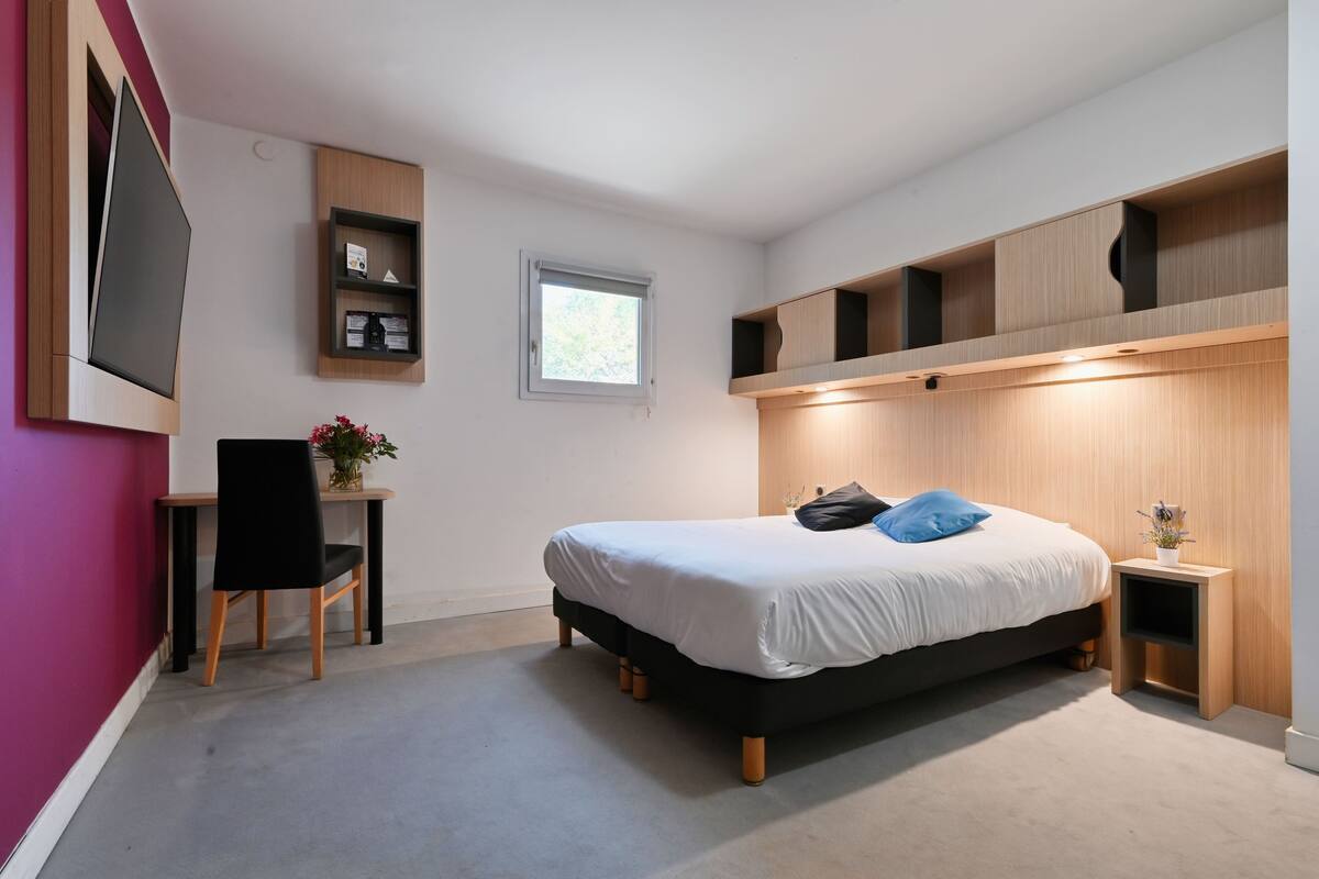 Une chambre à coucher moderne, équipée d’un lit, d’un bureau et d’un téléviseur fixé au mur.
