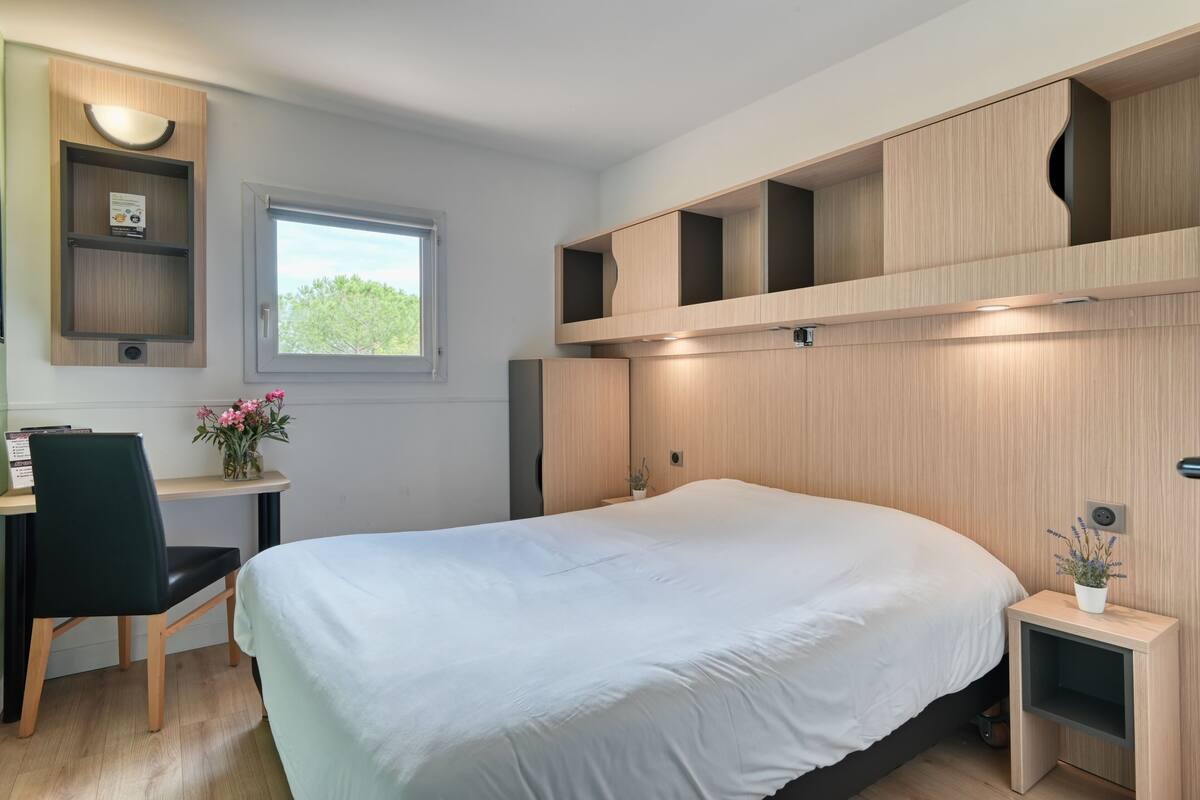 Une chambre moderne avec un grand lit, un bureau avec une chaise, une petite table agrémentée de fleurs et des étagères intégrées.