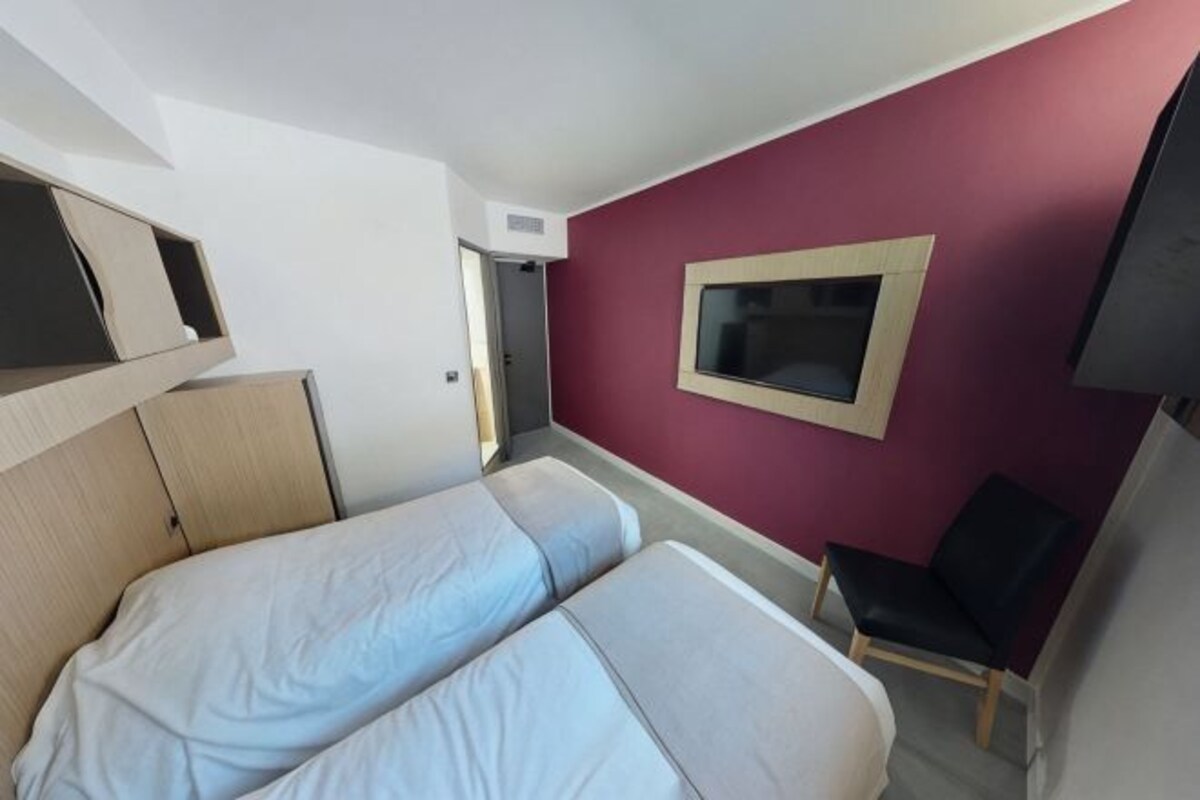 Una habitación con dos camas, una silla, un televisor y una puerta.