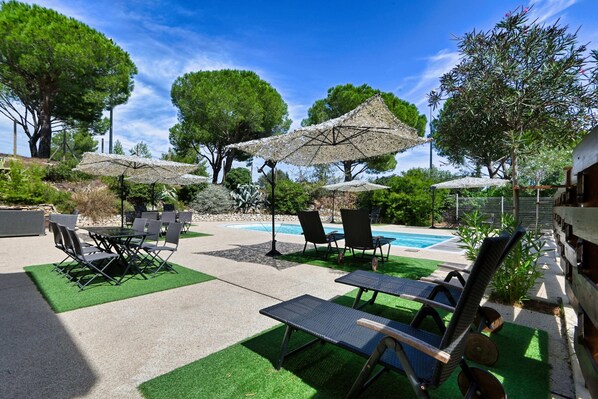 An outdoor pool area with lounge chairs, umbrellas, and a dining table. - La Villa Martégale (Martigues)