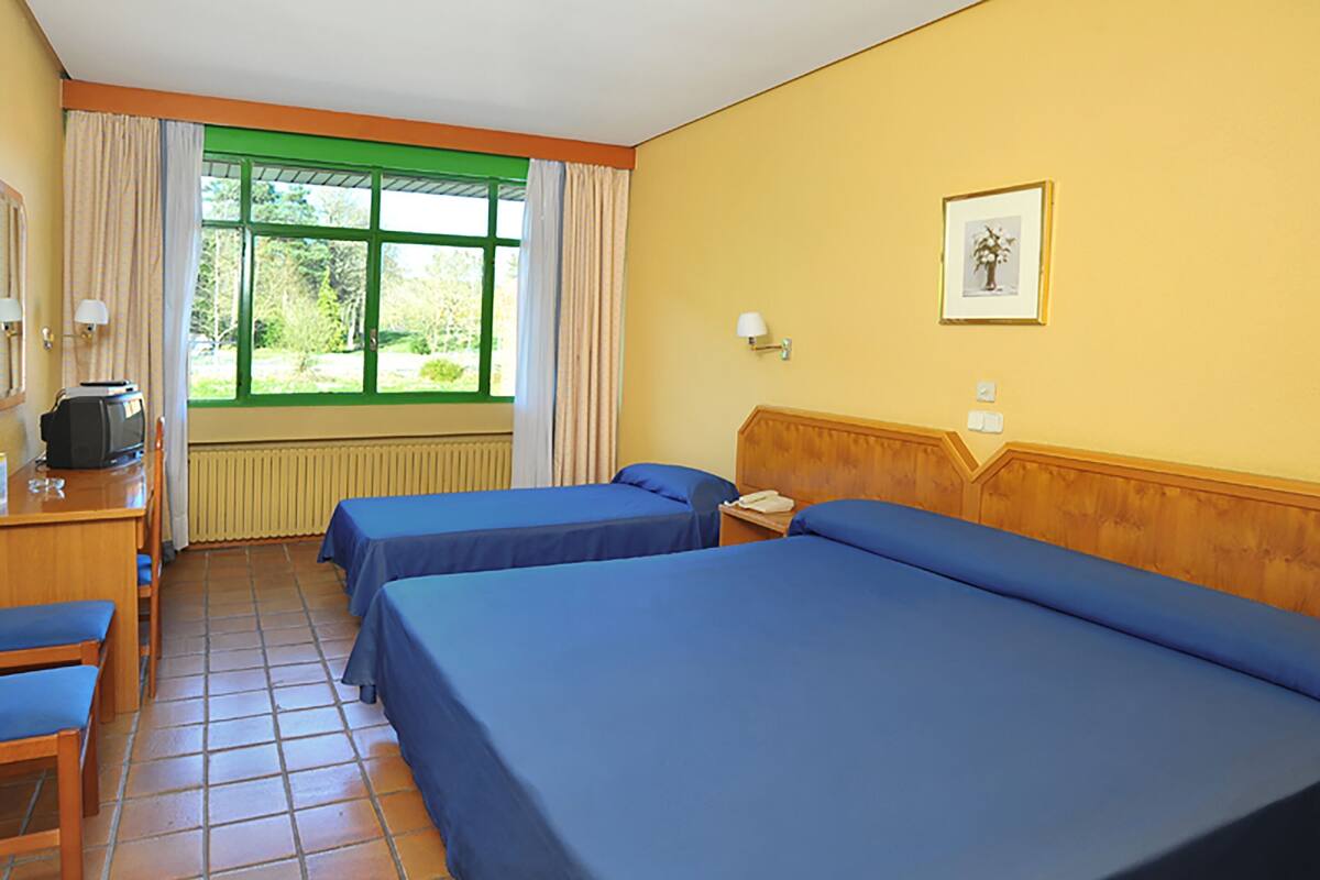 A hotel room with two beds, a desk, a chair, a television, and a window with curtains.