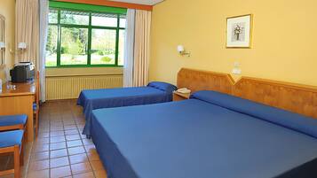 A hotel room with two single beds, a wooden desk with a chair, a television, and a window with curtains.