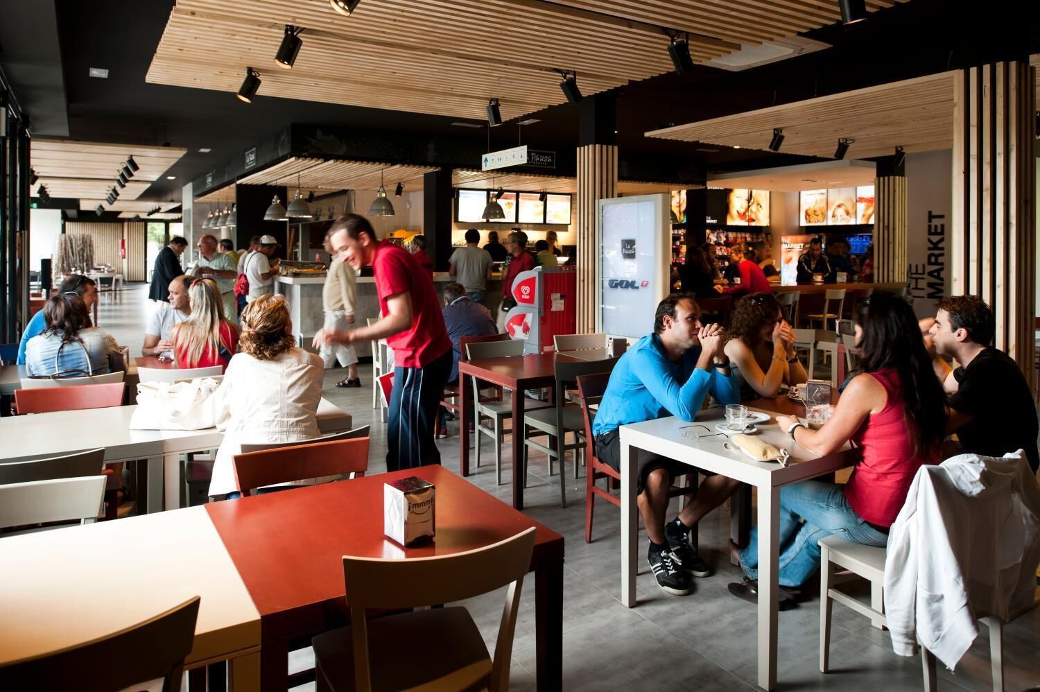 Een levendig restaurant met houten plafondpanelen, tafels en stoelen.