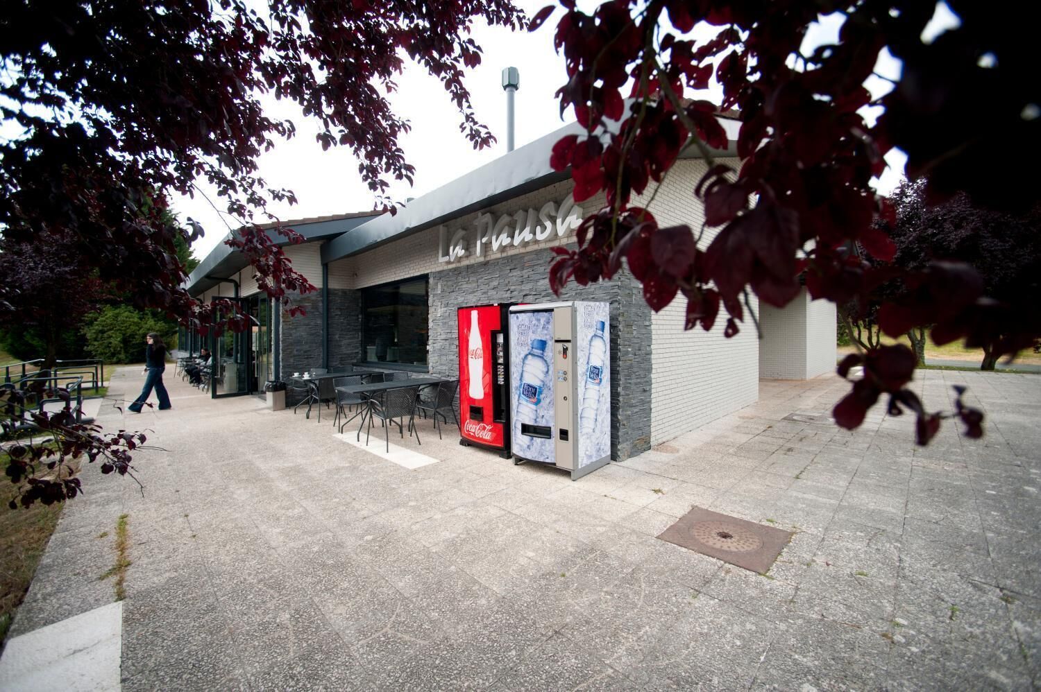 Een buitenruimte met tafels en stoelen, een Coca-Cola automaat en een gebouw met een stenen gevel.