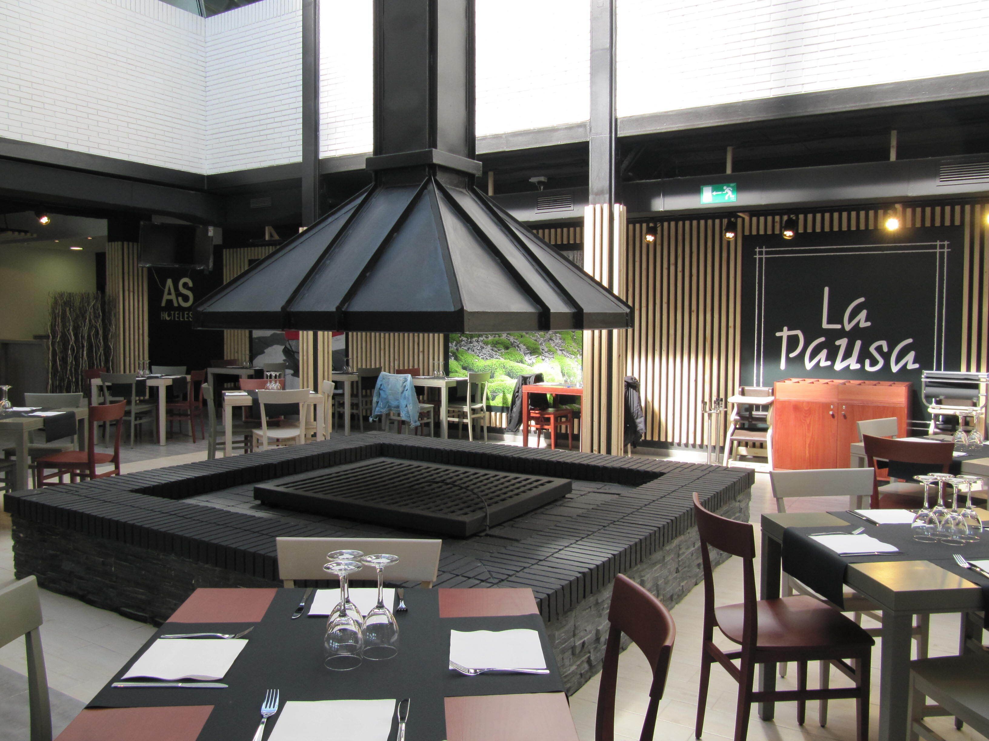 A restaurant with outdoor seating, a central fire feature, and a sign reading "La Pausa".