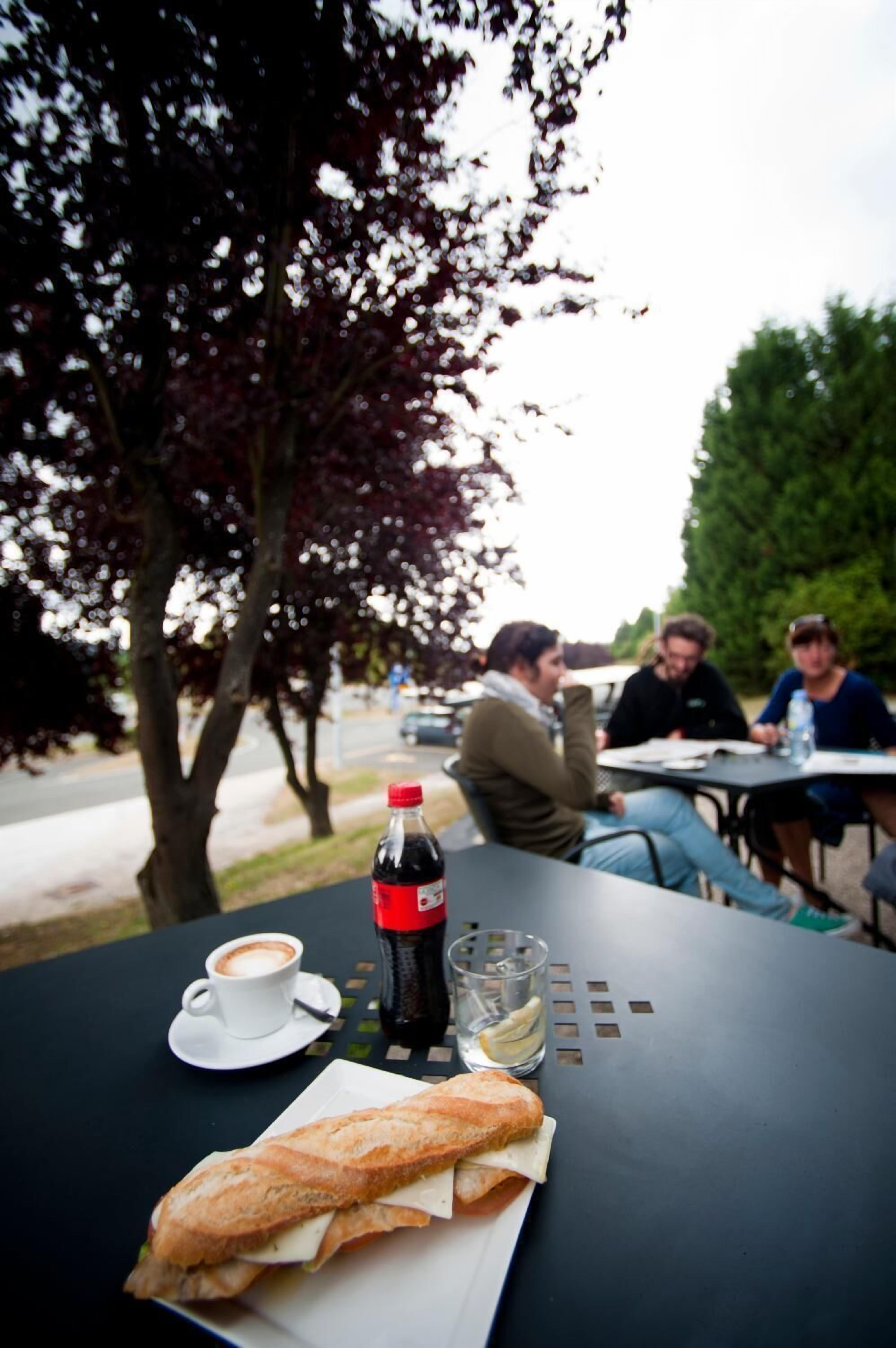 Une table avec un sandwich, une tasse de café, une bouteille de soda et un verre d’eau.