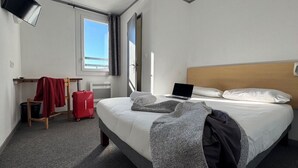 Une chambre d’hôtel avec un lit, un ordinateur portable, une télévision, une fenêtre et une valise rouge.