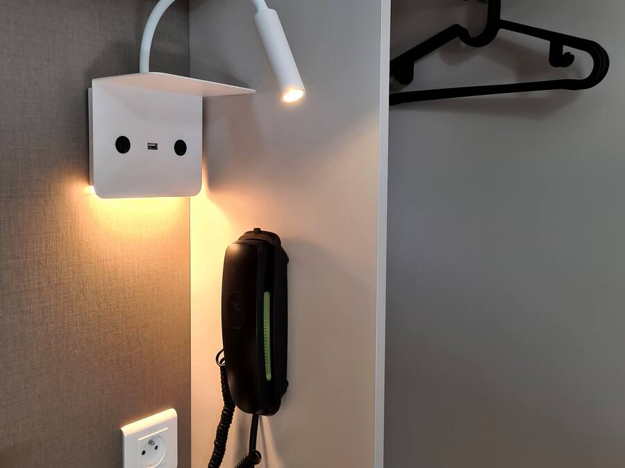 Una toma de corriente fijada en la pared, un tapón blanco, un dispositivo negro con una luz verde y un interruptor blanco debajo.