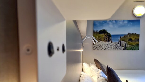 Een bed met witte beddengoed en een schilderij van een strandlandschap aan de muur.