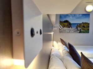 Ein Bett mit weißer Bettwäsche und einem Gemälde einer Strandansicht an der Wand dahinter.