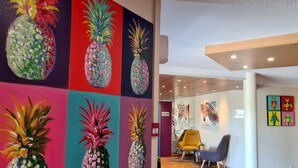 Een gang met kleurrijke ananas schilderijen aan de muren, een houten vloer en moderne stoelen.