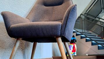 A modern armchair with wooden legs, positioned on a wooden floor with a textured rug.