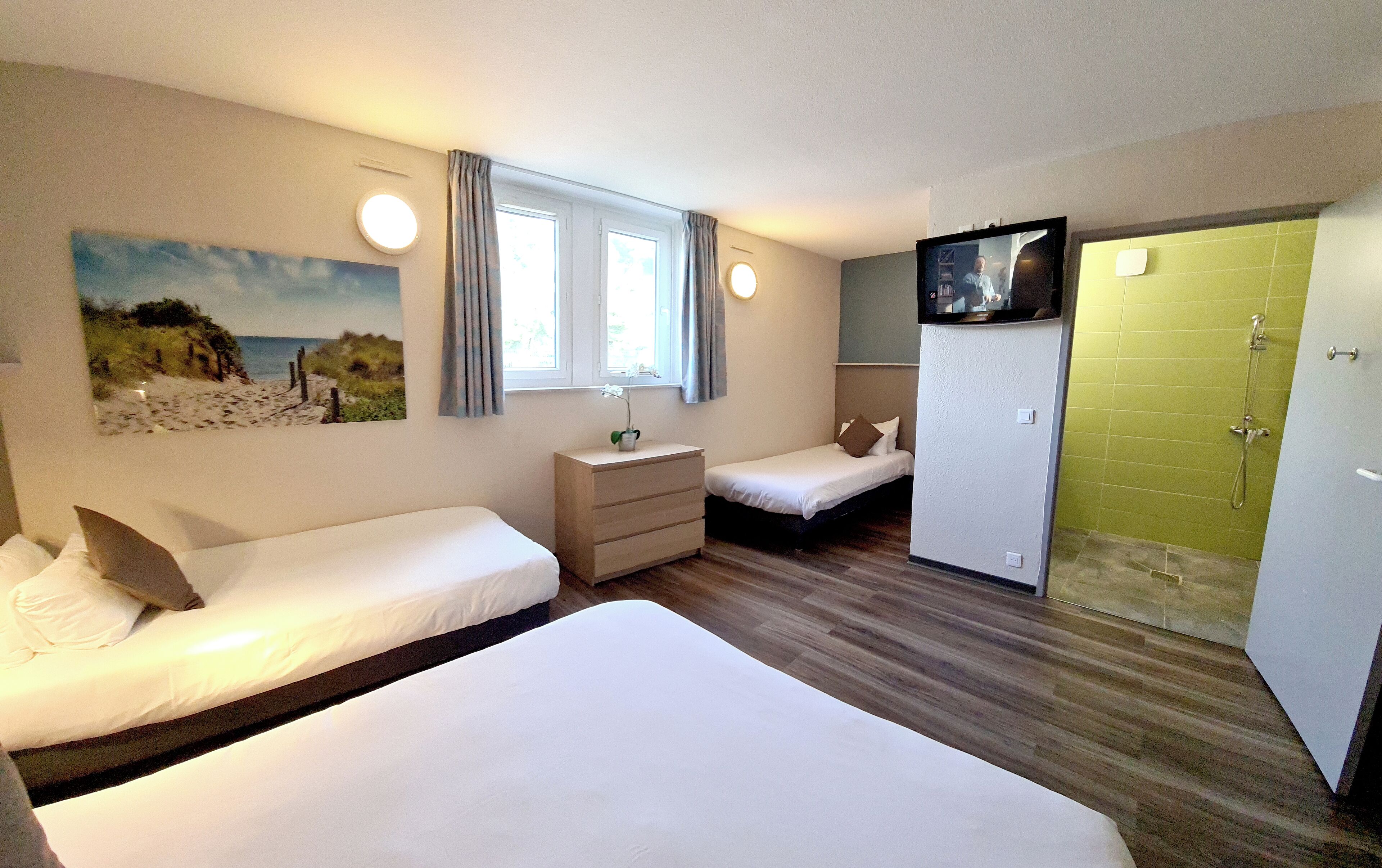 Et hotelværelse med to senge, en kommode, et fjernsyn og et badeværelse med bruser.