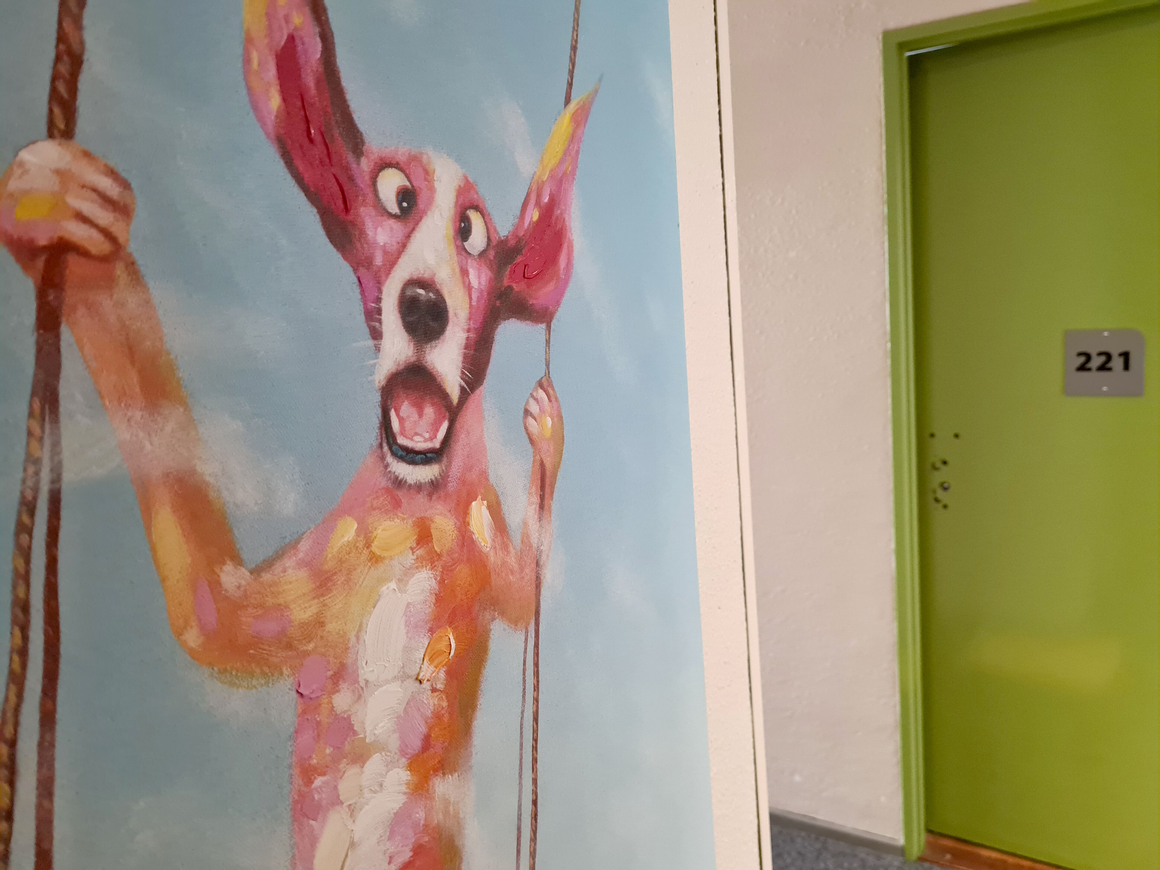 Un mural en la pared con un perro sosteniendo una cuerda, una puerta verde con el número 221 y una pared blanca.