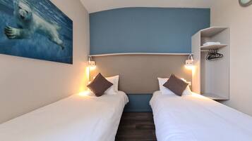 A hotel room with two single beds, a headboard, bedside lamps, a painting of a polar bear, and a small shelf with a hanger.