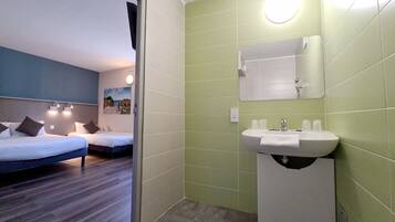 A hotel room with two beds, a bathroom with a sink and mirror, and a view of the beach through the window.