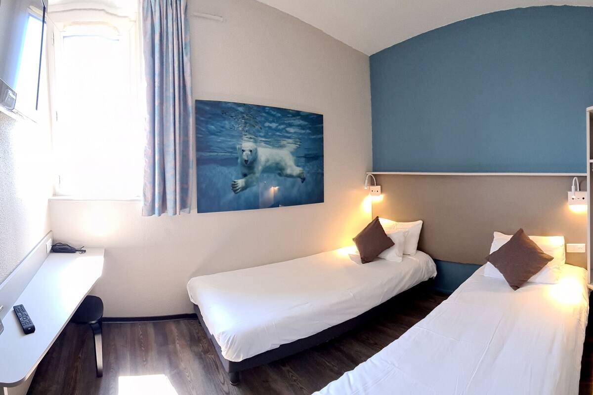 Habitació d'hotel amb dos llits, una taula de treball, un quadre d'un óss polar, dutxa i una petita estant amb tovalloles.